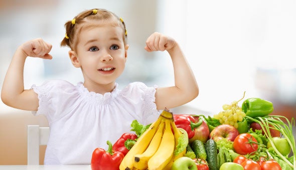 Niña fuerte junto a diferentes frutas y verduras